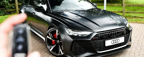 Mão segurando a chave de um Audi preto recém-comprado com consórcio de carro