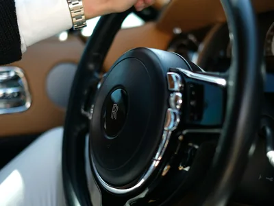 Mão com relógio ao volante de um carro de luxo com interior em couro claro
